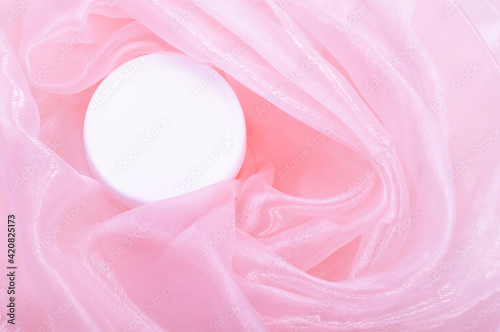 White cream jar on a background of pink silk fabric..Flat lay, top view, copy space. Natural organic product, beauty and spa concept. Rose cosmetics White cream jar on a background of pink silk fabric..Flat lay, top view, copy space. Natural organic product, beauty and spa concept. Rose cosmetics