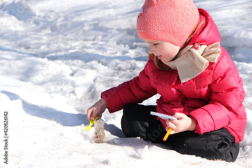Canvas Print Little girl in warm winter clothes with notepad and pen in her hand investigate details of nature and experimenting with dry plants snow and laboratory flask