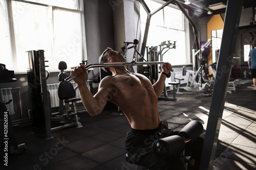 Male athlete with strong muscular torso exercising on lat pull down gym machine photo