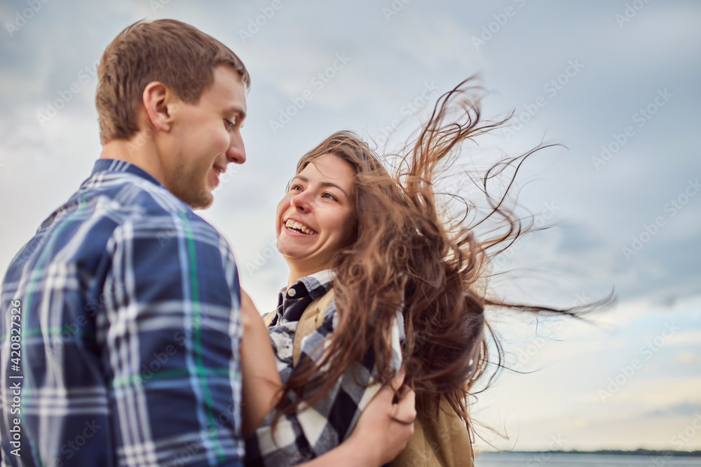 Lovers in a lake. Young couple in love sitting on the park ground near the water while these young man playing guitar in sunset time. Lovers in a lake. Young couple in love sitting on the park ground near the water while these young man playing guitar in sunset time.