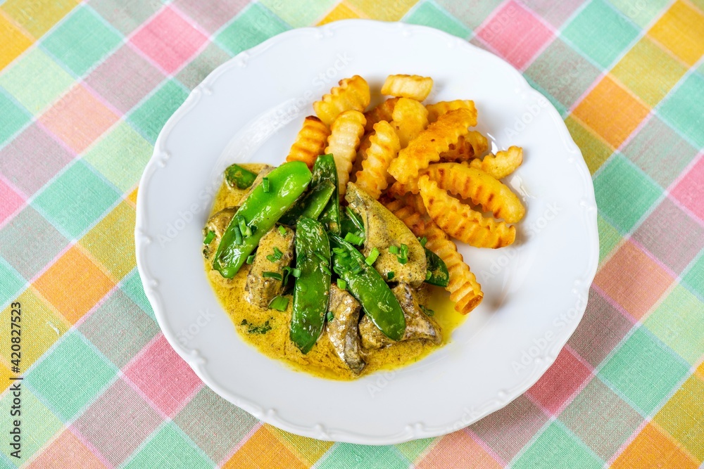 Roasted liver in curry sauce with green sweet pea pod and french fries.