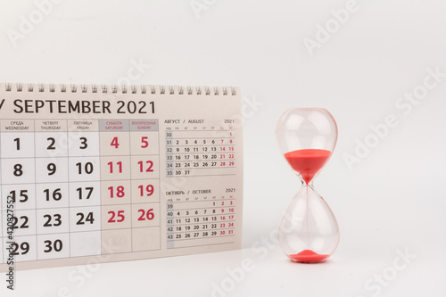 Time passing concept. Crystal hourglass with red sand and calendar on light background