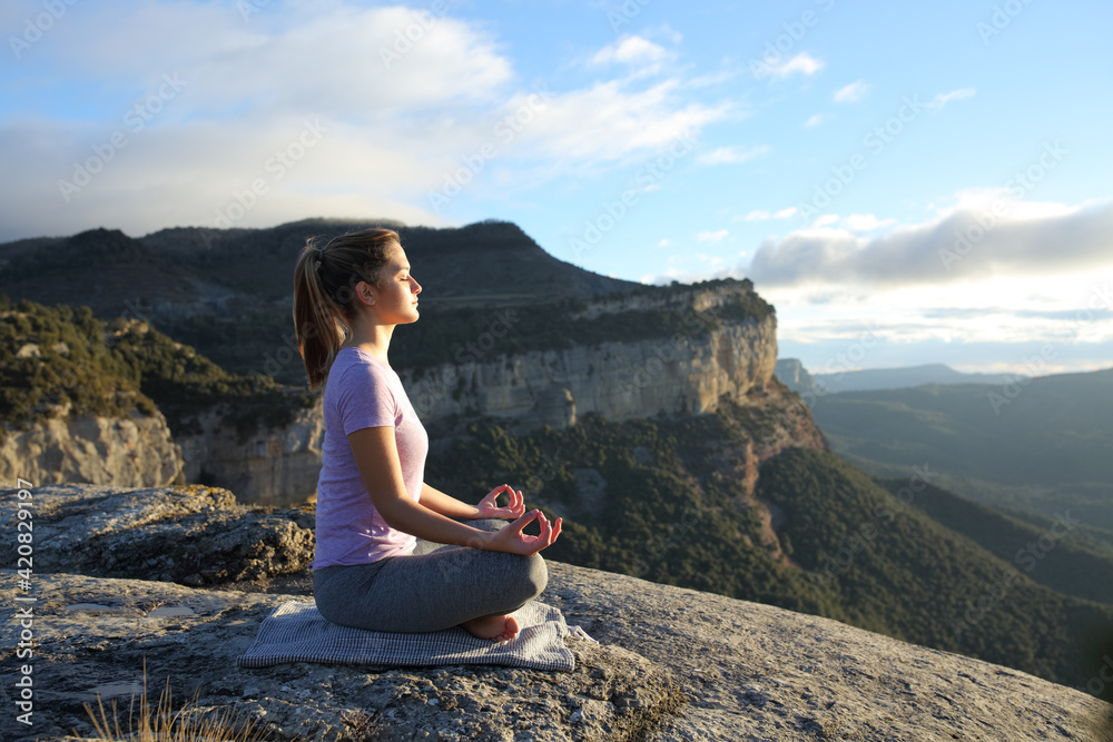 Profile of a woman doing yoga in the top of a cliff
