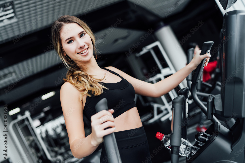 Athletic blonde girl during a workout on a cardio machine, smiling, looks at the camera