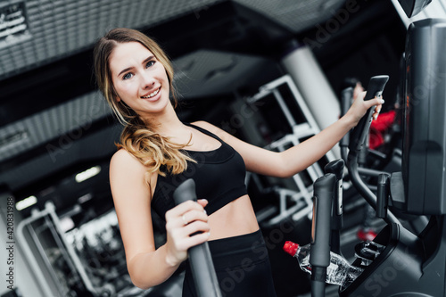 Athletic blonde girl during a workout on a cardio machine, smiling, looks at the camera