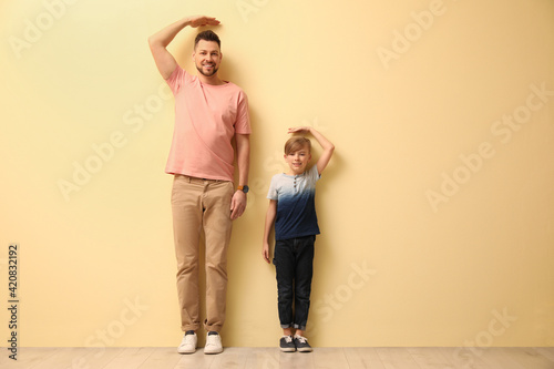 Father and son comparing their heights near beige wall indoors. Space for text