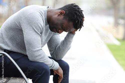 Sad black man is complaining alone in a park photo