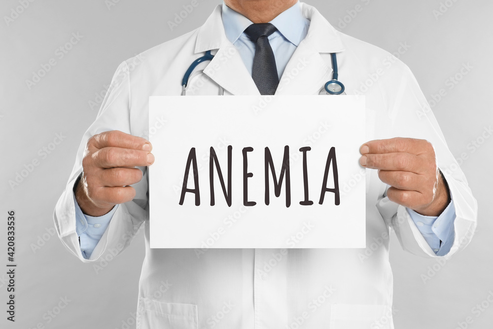Doctor holding sign with word ANEMIA on light grey background, closeup Doctor holding sign with word ANEMIA on light grey background, closeup