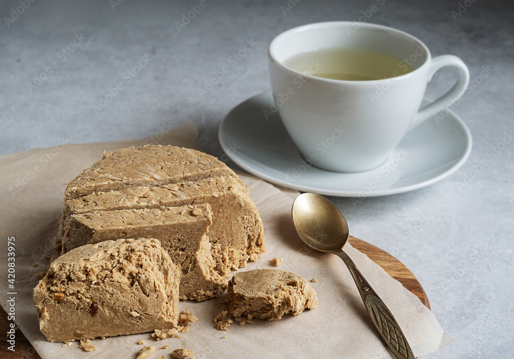 Halva sunflower - sweet dessert and green tea in a white cup on a light background. Selective focus. Halva sunflower - sweet dessert and green tea in a white cup on a light background. Selective focus.
