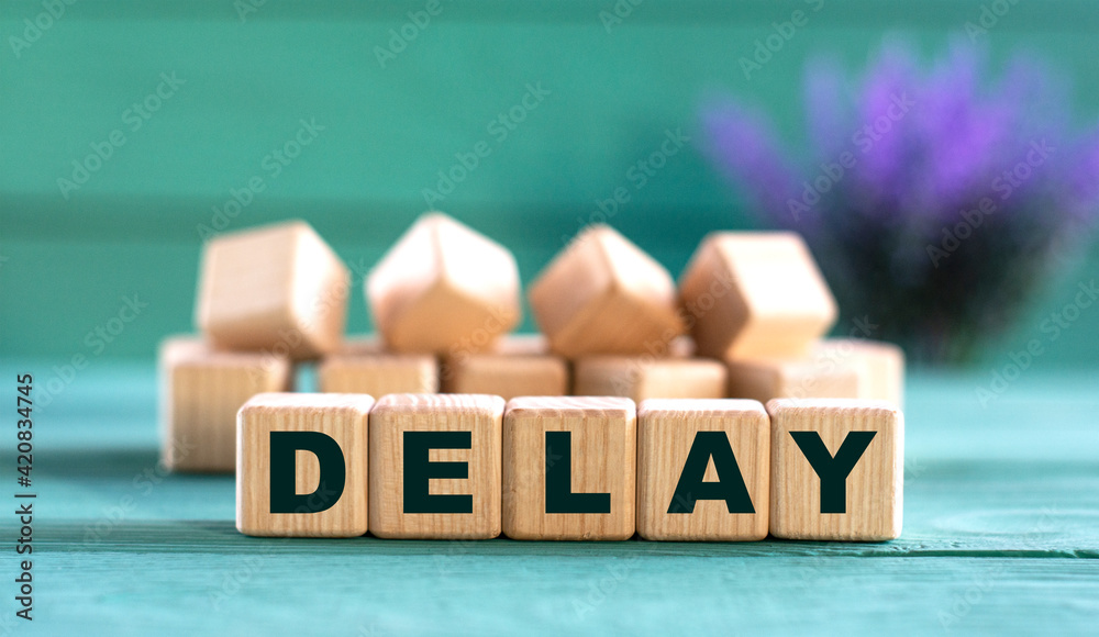 DELAY - word on wooden cubes on a green background with lavender DELAY - word on wooden cubes on a green background with lavender