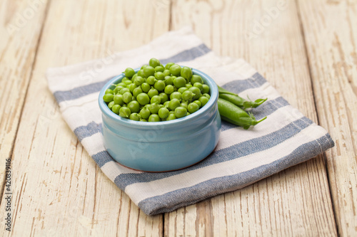 Green peas in ceramic bowl on white wooden table background