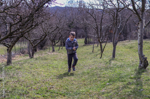 Boy is playing and running across a meadow through an alley in nature on an early spring day in the countryside © Emilija