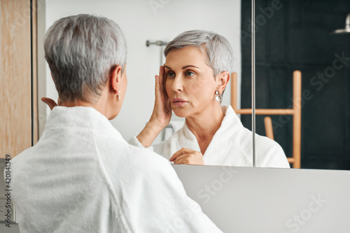 Фотография Senior female touching her face in a bathroom