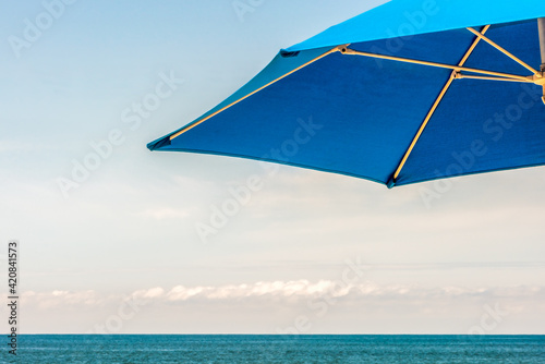 Idyllic tropical holiday image, bright blue beach umbrella with the horizon over the ocean