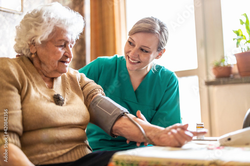 Female caretaker measuring senior woman's blood pressure at home
 photo