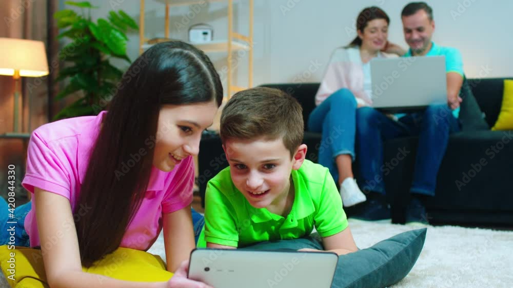 At home on the soma happy parents using laptop to watch something together while kids using tablet to play some games At home on the soma happy parents using laptop to watch something together while kids using tablet to play some games