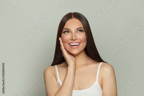 Happy surprised brunette model woman with clear skin and long healthy straight hair on white. Skincare and facial treatment concept