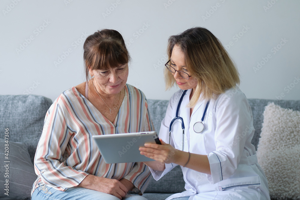 Female professional doctor showing medical test result explaining prescription using digital tablet app visiting senior woman patient at home sitting on sofa. Elderly people healthcare tech concept. Female professional doctor showing medical test result explaining prescription using digital tablet app visiting senior woman patient at home sitting on sofa. Elderly people healthcare tech concept.