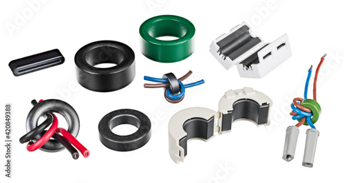 Set of electronic ferrite bead chokes isolated on white background. Various clamp-on magnetic cores or rings with wrapped insulated wires. EMI filter inductors prevent high-frequency electronic noise.