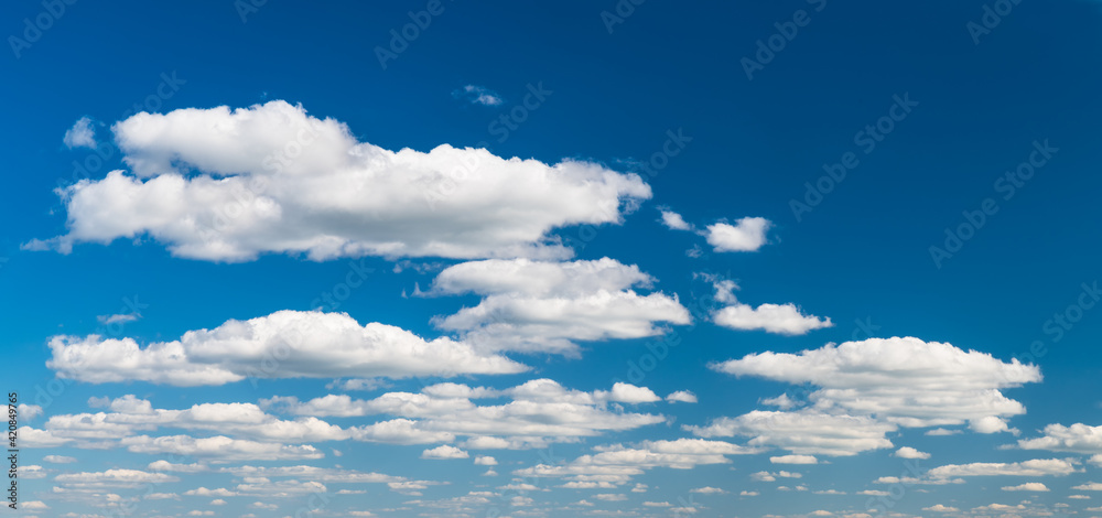 Group of idyllic floating white clouds on azure blue sky background. Tranquil natural panoramic cloudscape scene with copy space in top right corner. Environment or ecosystem, weather and meteorology.