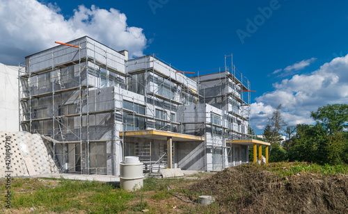 New residential house exterior under construction on building site. Summer blue sky. Modern urban apartments with unfinished facade and metal pipe scaffolding. Architecture or real estate development.