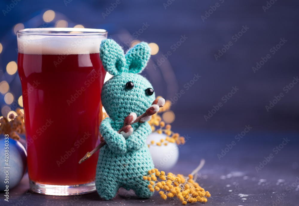 A glass of beer on the table with Easter eggs, a copy space card. Easter knitted rabbit, soft toy - obrazy, fototapety, plakaty 