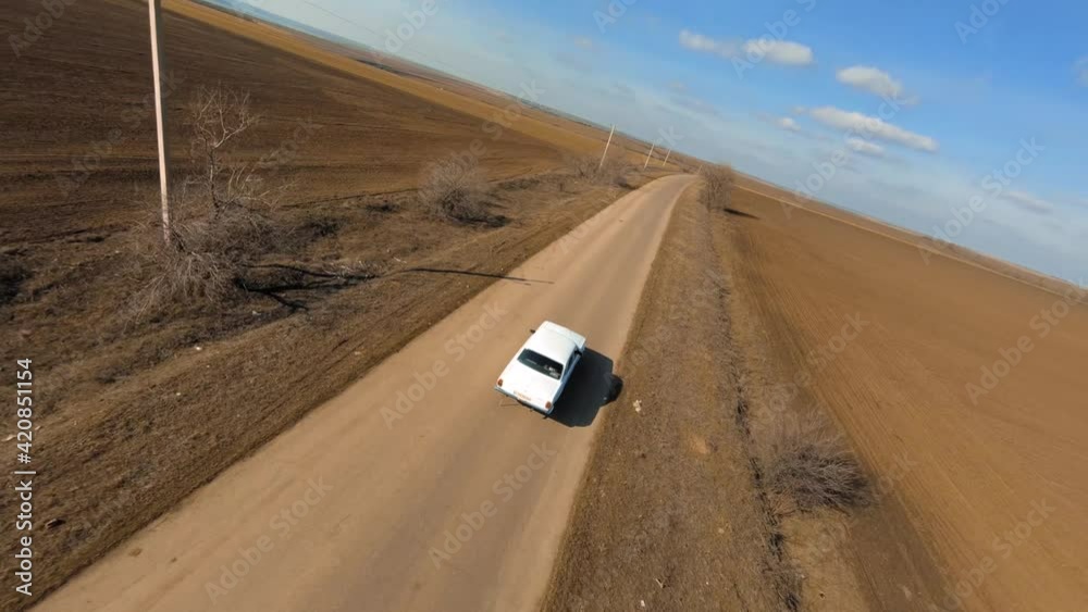 Fpv sport drone with action camera follows Old Soviet Car Volga 24 on the Lonely Road Between Brown Fields. Fpv Racing drone first Person cinematic chase view.