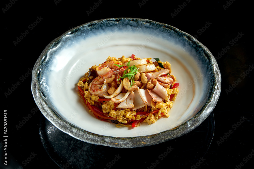 Glass rice noodles in sweet and sour sauce with shrimp, scallops, octopus and squid, served in a white bowl. Wok noodles. Isolated on a black background. Street thai food Glass rice noodles in sweet and sour sauce with shrimp, scallops, octopus and squid, served in a white bowl. Wok noodles. Isolated on a black background. Street thai food