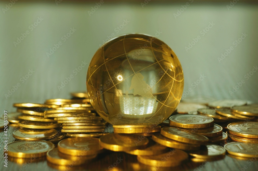 A small glass globe with coins on a colored background.