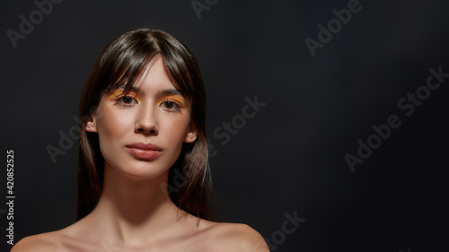 Close up portrait of beautiful young brunette woman with big brown eyes and colorful makeup smiling at camera, posing isolated over black background