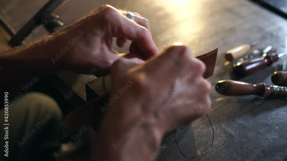 Man sews leather details clamped in vice. Craftsman works with needle and thread. Man sews leather details clamped in vice. Craftsman works with needle and thread.
