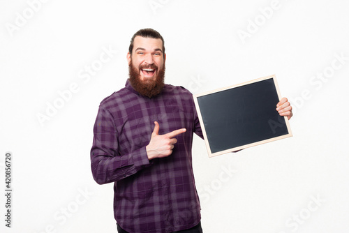 Hey look at this, amazed bearded man in casual pointing at empty black chalk board