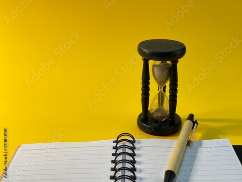 On a yellow background there is an hourglass measuring the time, next to it is a pen and an open notebook