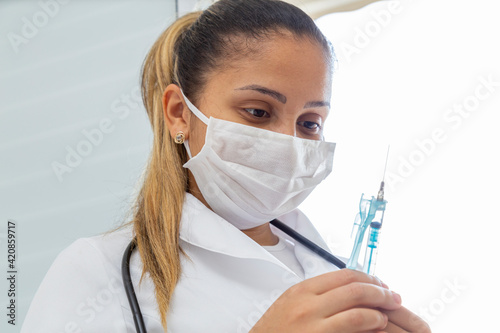 Female doctor with mask and holding syringe with needle.