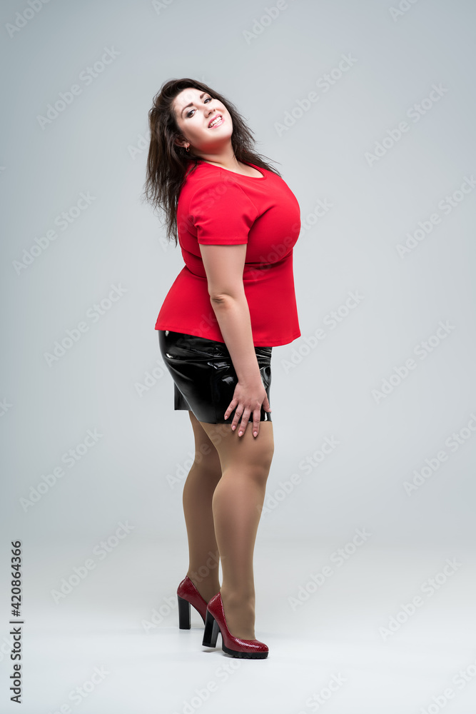 Happy plus size fashion model in red blouse and black skirt, fat woman on gray background, body positive concept Happy plus size fashion model in red blouse and black skirt, fat woman on gray background, body positive concept