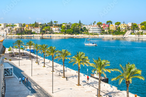The harbor port of the waterfront city of Brindisi, Italy, in the southern Puglia region on a sunny summer day with palm trees lining the boardwalk.