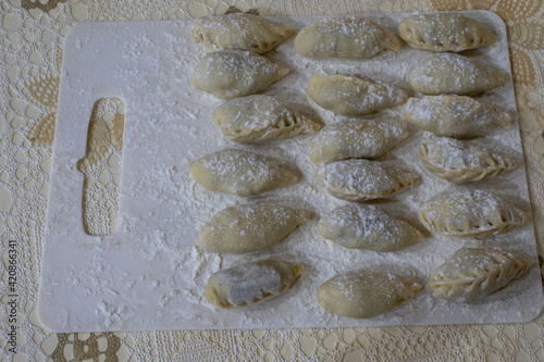 Uncooked russian pelmeni on cutting board and ingredients for homemade pelmeni on white table. Process of making pelmeni, ravioli or dumplings with meat. Raw meat in dough on a cutting board