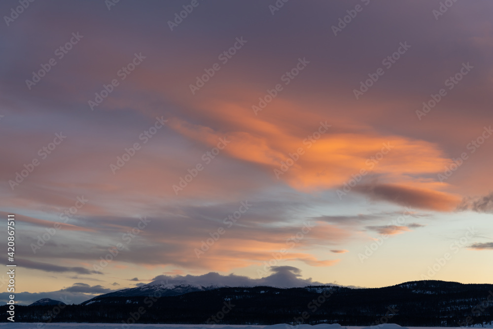 A fiery orange, pink and purple dark sunset seen in northern Canada during winter time season with snow capped mountains and wilderness setting landscape for prints, art, office or home artwork. 