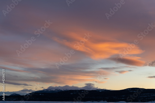 A fiery orange  pink and purple dark sunset seen in northern Canada during winter time season with snow capped mountains and wilderness setting landscape for prints  art  office or home artwork. 