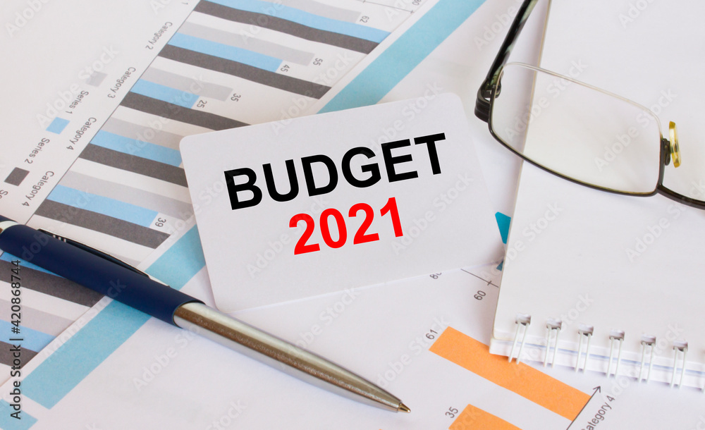 Business card with text Budget 2021 lies on financial charts with pen and eyeglass Business card with text Budget 2021 lies on financial charts with pen and eyeglass