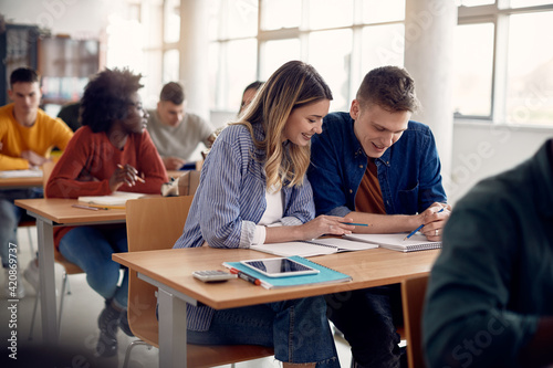 Happy university students reading lecture from notebook in lecture hall.