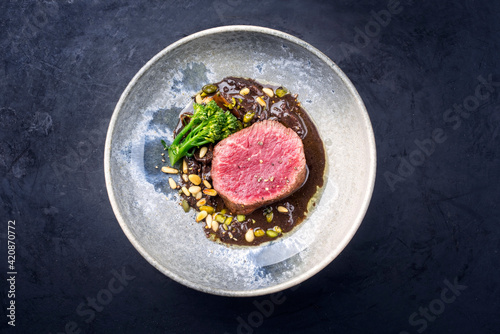 Modern style barbecue dry aged angus beef filet steak natural with broccolini and truffle mushroom sauce served as top view on a design plate with copy space