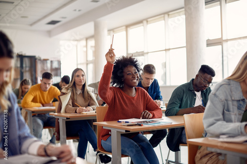 Carta da parati Happy black student raising arm to answer question while attending class with her university colleagues