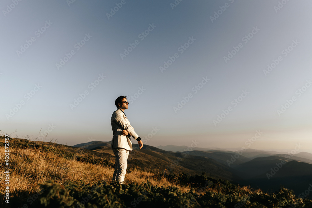 Handsome man in glasses and a light beige suit walks in the mountains Handsome man in glasses and a light beige suit walks in the mountains