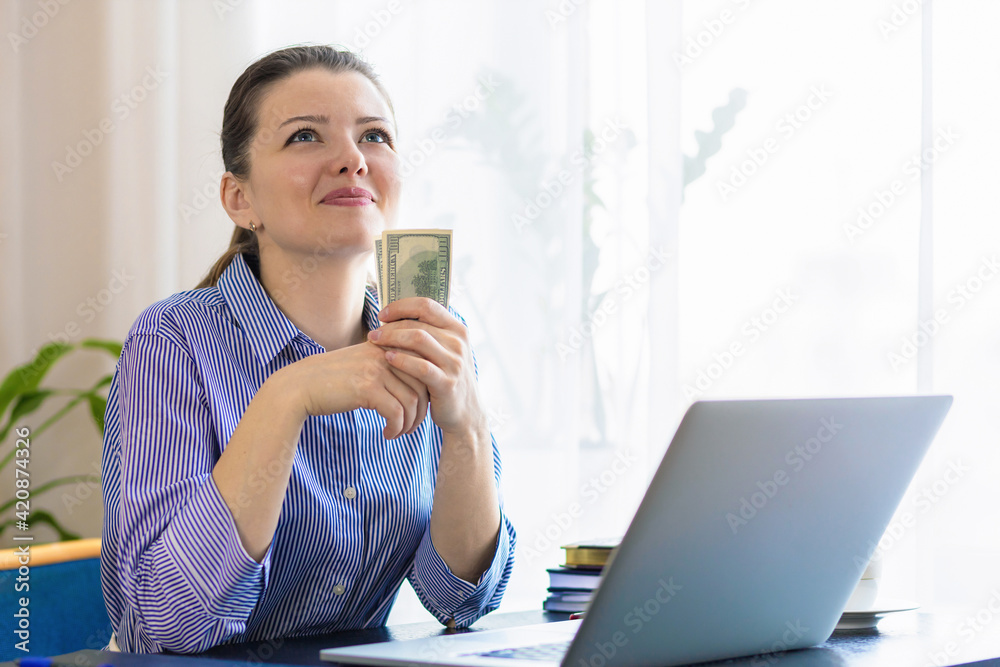 happy woman at laptop, working remotely, successful online business, wad of dollar cash, dreaming, thinking about future purchases, spend the money. planning budget, holding banknotes. lottery win