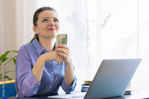 Fotografie happy woman at laptop, working remotely, successful online business, wad of dollar cash, dreaming, thinking about future purchases, spend the money