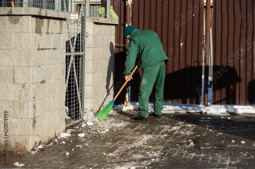 A manual worker sweeps the remnants of snow off a wet pavement with a broom © fotodrobik