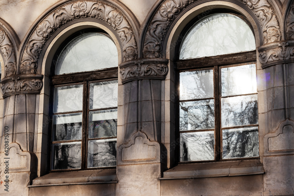 The image of two symmetrical windows whose frames have a special architecture and in which the trees outside are reflected The image of two symmetrical windows whose frames have a special architecture and in which the trees outside are reflected