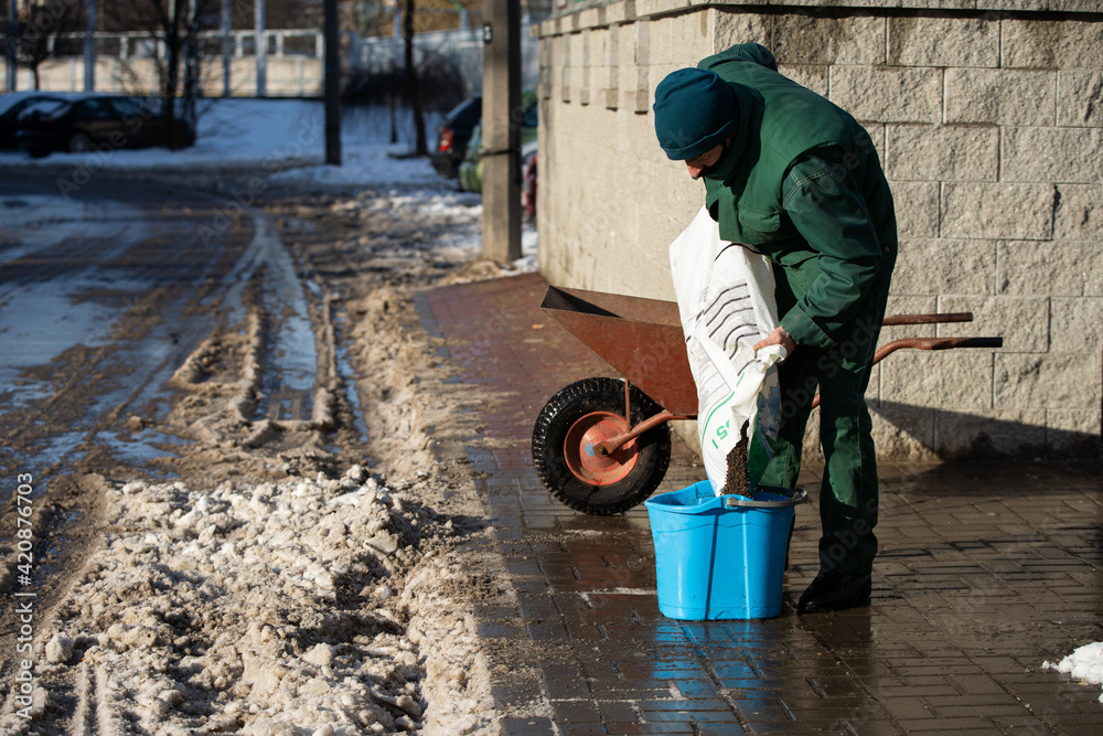 An employee pours expanded clay from the bag into a bucket, which he will use to sprinkle pavements An employee pours expanded clay from the bag into a bucket, which he will use to sprinkle pavements