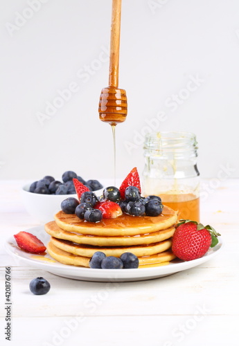 Still life with pancakes, berries and honey on a white background